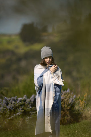 Una ragazza in un parco, si ripara dal freddo stringendosi addosso un plaid ed indossando un cappello Cecchi e Cecchi