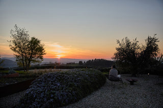 Una ragazza seduta in giardino guarda il tramonto coperta da un plaid Cecchi e Cecchi