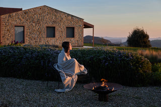 Una ragazza in giardino, di fronte ad un braciere, si stringe addosso una coperta Cecchi e Cecchi