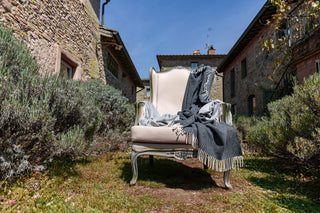 Dei plaid con frange in pura lana vergine appoggiati su una sedia all'esterno di una casa toscana